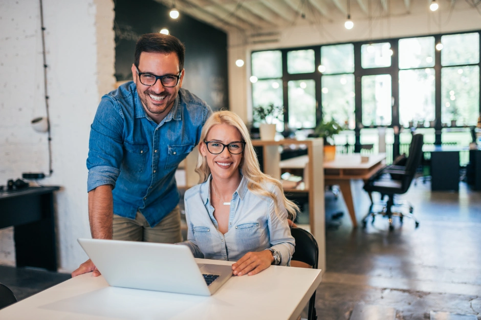Two smiling business professionals working together on a laptop to build business credit in a modern office.