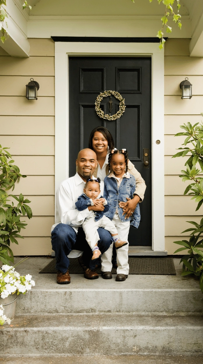 A smiling family of four posing in front of their home's front door after using CPN packages for housing.