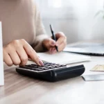 A person using a calculator at a desk with credit cards, a notebook, and a calendar nearby, illustrating concepts related to financial planning and CPN tradelines for sale.